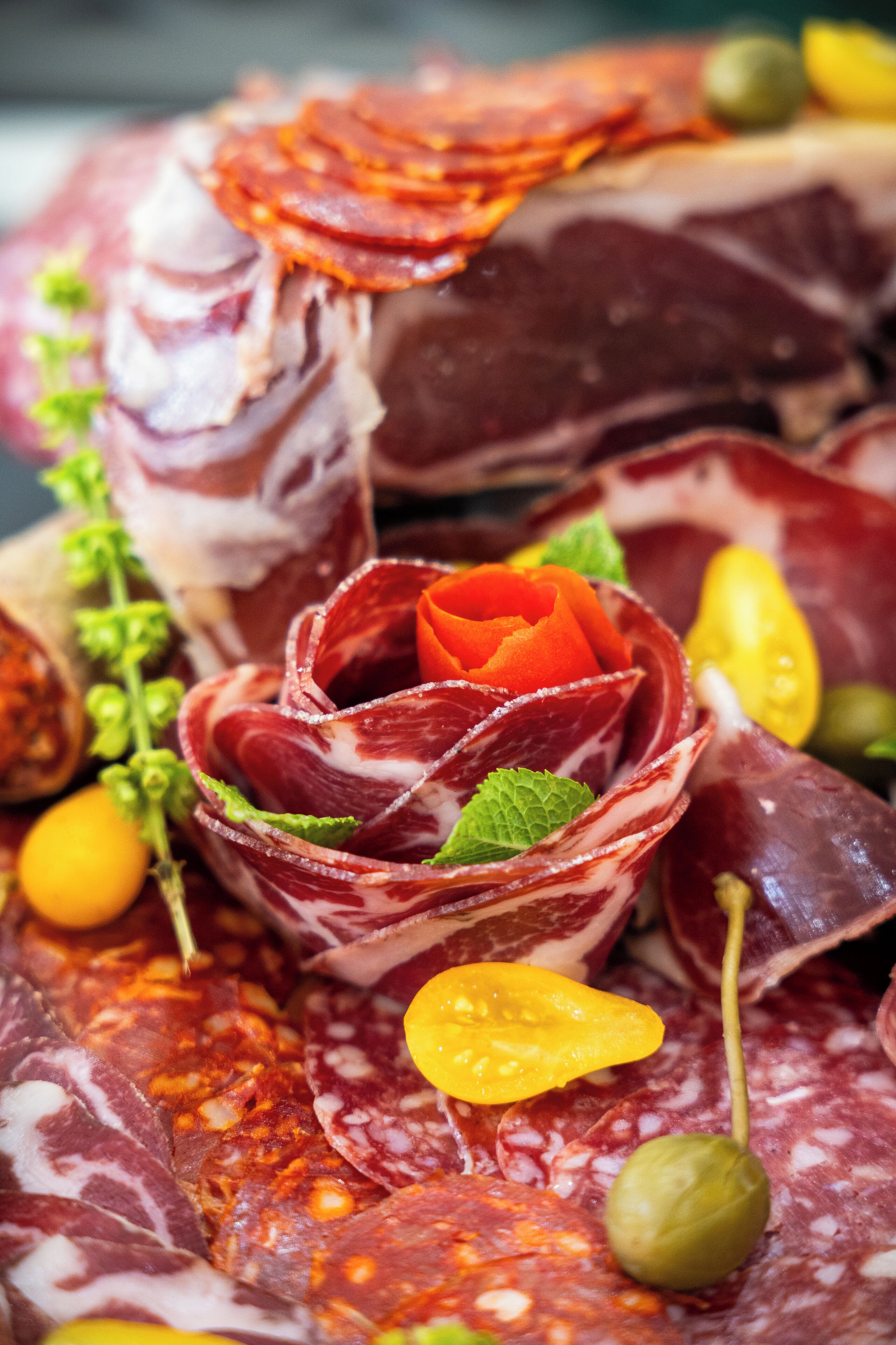 A charcuterie board with various meats, olives, and a decorative flower.