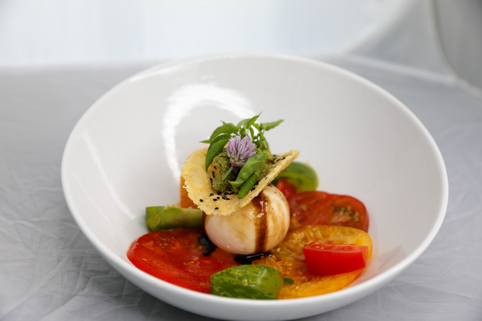 Un tazón blanco con un plato de vieiras, verduras y una hierba decorativa.
