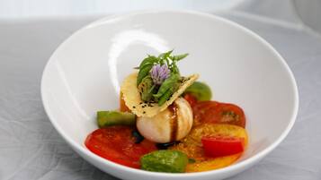 Un tazón blanco con un plato de vieiras, verduras y una hierba decorativa.