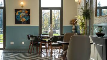 Un comedor con una mesa y sillas, un ventanal con vistas a árboles, y una lámpara fijada a la pared.