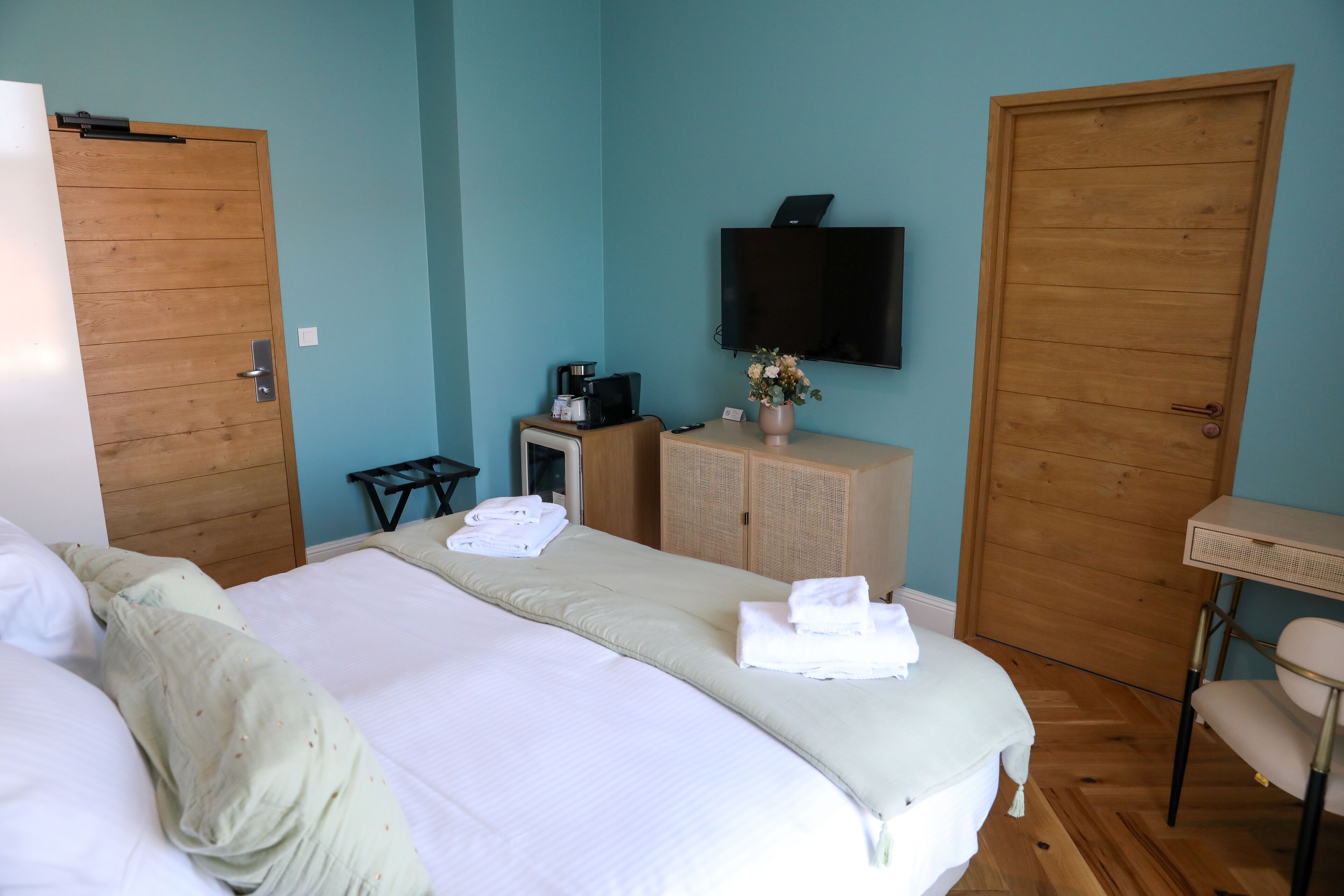 A hotel room with two beds, a television mounted on the wall, a desk with a chair, and wooden doors.