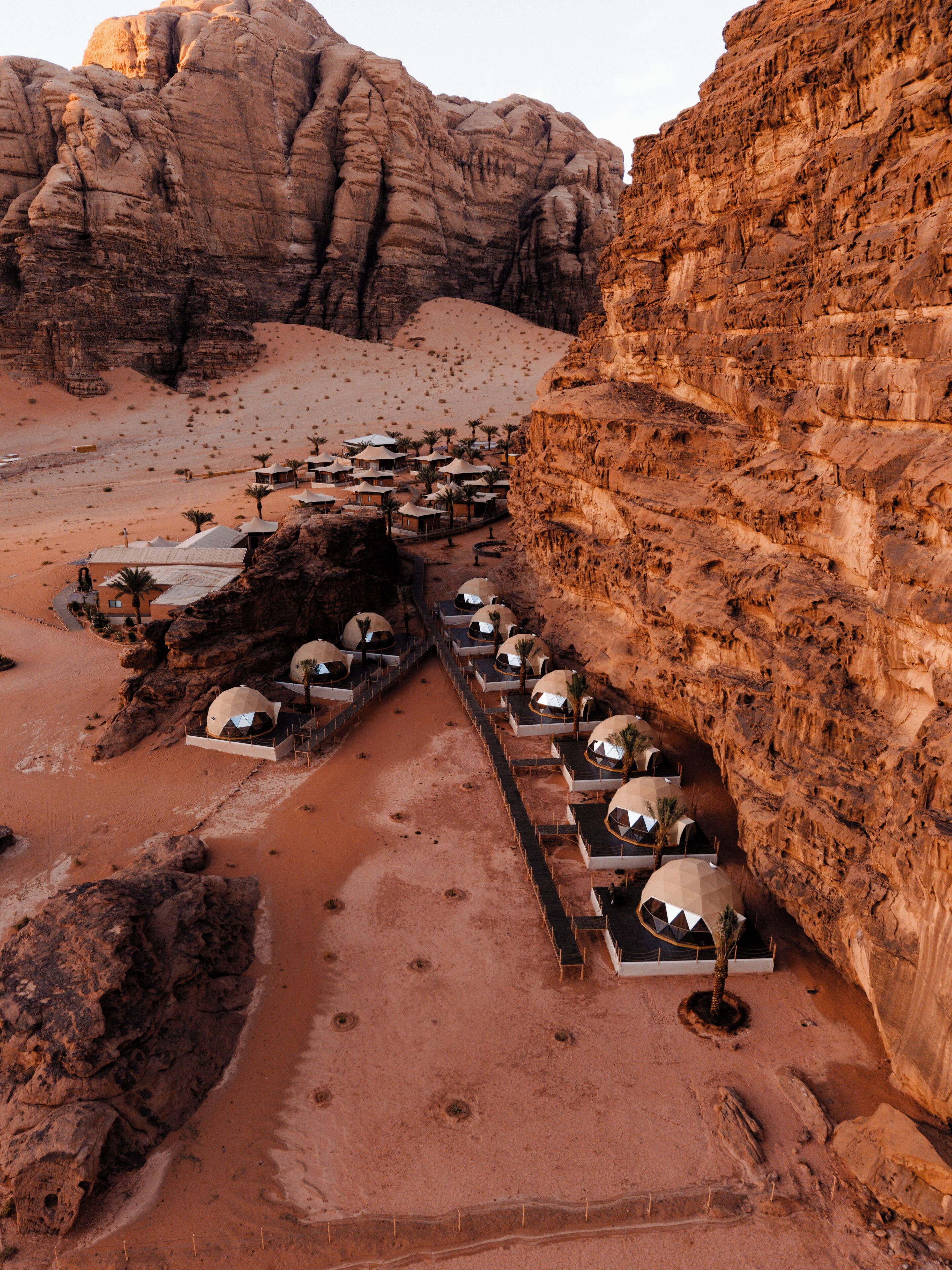 A desert resort with dome-shaped accommodations aligned along a pathway, surrounded by rocky cliffs.