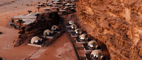 A desert resort with dome-shaped accommodations aligned along a pathway, surrounded by rocky cliffs.
