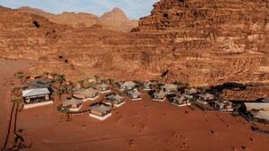 Un complexe hôtelier situé dans le désert, composé de plusieurs tentes et bordé de palmiers.