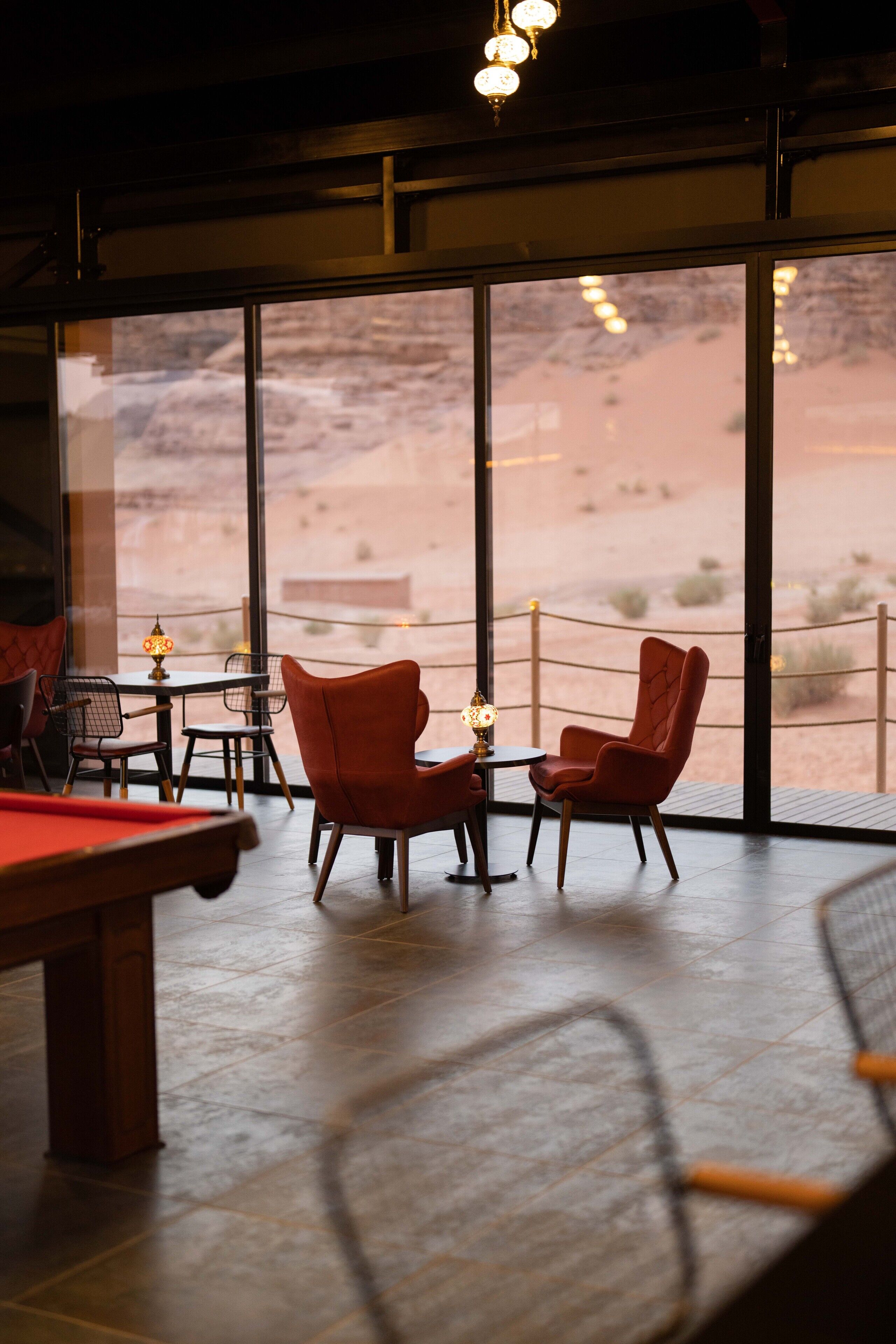 A pool table in a room with large windows, two chairs, and a lamp.