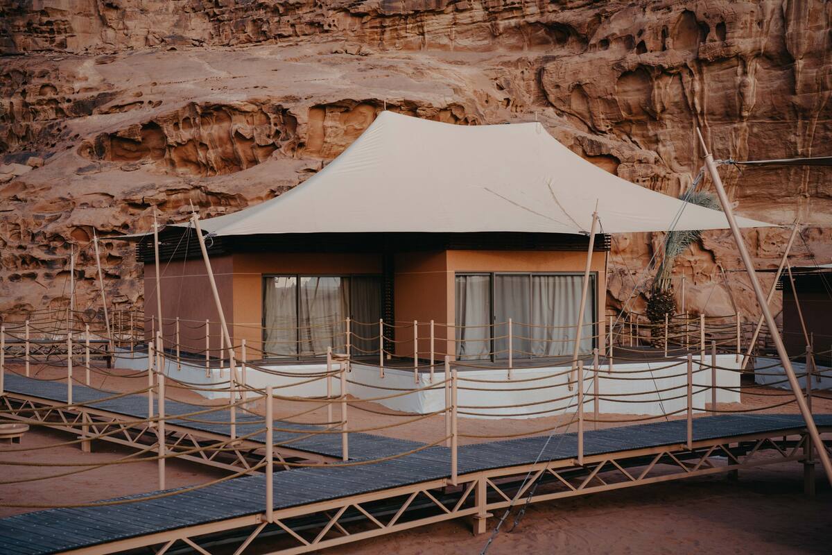 A desert resort with a large white tent structure, wooden walkways, and a rocky backdrop.