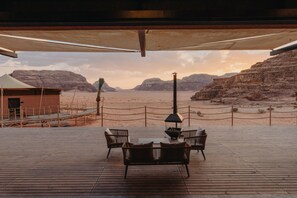 A wooden deck with outdoor furniture, a barbecue grill, and a view of a desert landscape with rocky hills. - Valley Resort (Wadi Rum)