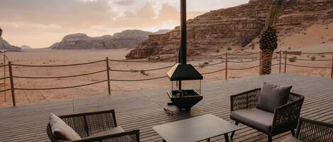 A deck with wicker furniture, a table, and a fire pit, overlooking a desert landscape with rocky hills.