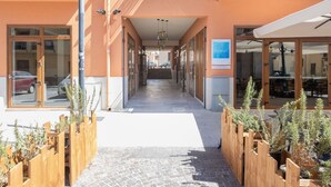 Ein Korridor mit Holzpflanzgefäßen, Glastüren und einem gefliesten Boden, der zu einem Restaurantbereich führt.