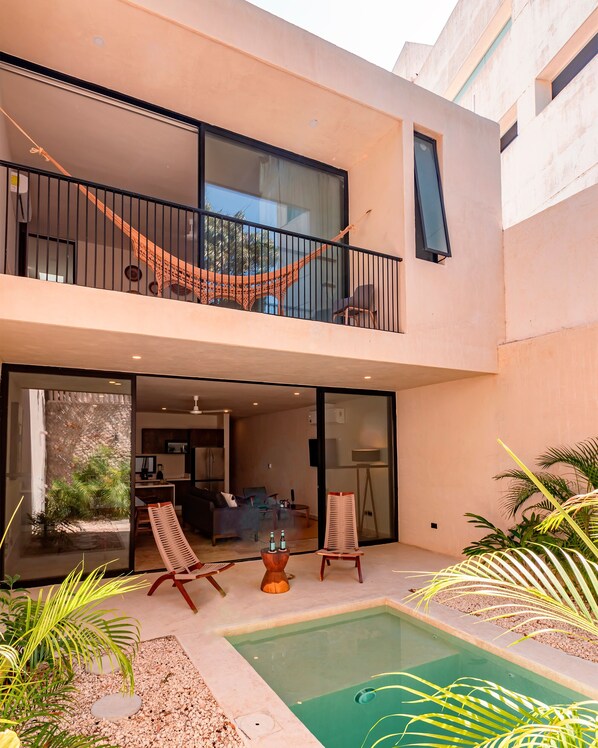 A modern two-story house with a balcony, a pool, and a dining area.