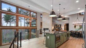 Une cuisine spacieuse dotée d’un grand îlot central, de planchers en bois et offrant une vue sur les arbres grâce à de grandes fenêtres.