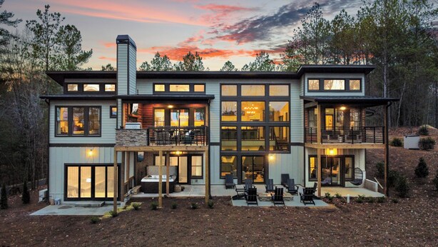 Une maison moderne à deux étages, dotée de grandes fenêtres, d’une cheminée en pierre et d’un espace salon extérieur.