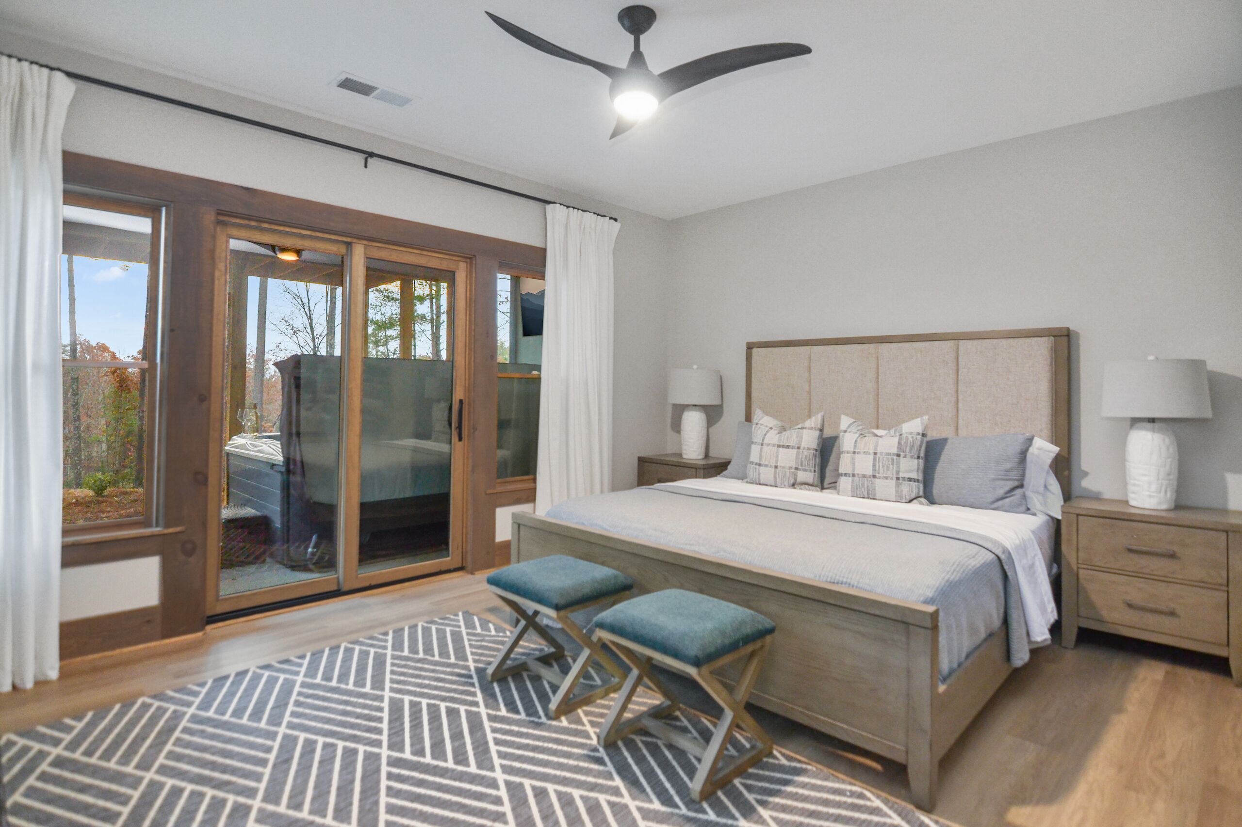 A bedroom with a large bed, two nightstands, a ceiling fan, and a sliding glass door leading to a balcony.