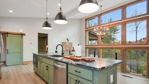 Une cuisine dotée d’un grand îlot central, de meubles de couleur verte et offrant une vue dégagée grâce à de grandes fenêtres.