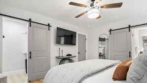 A bedroom with a bed, a ceiling fan, a TV, and a door with a sliding barn door.