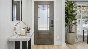 A modern entryway with a wooden door, a marble console table, a large potted plant, and a large mirror on the wall.