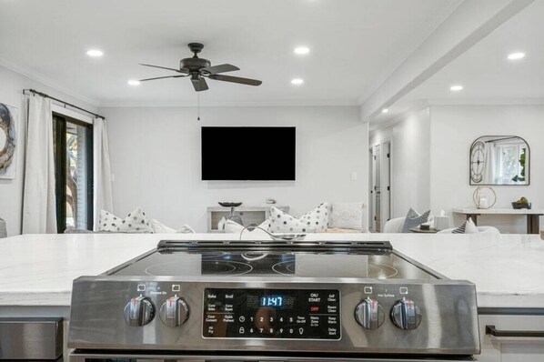A modern kitchen with a built-in gas stove, a ceiling fan, and a large flat-screen TV mounted on the wall. - Sunny Escape Complete Reno W/Pool (Tulsa)
