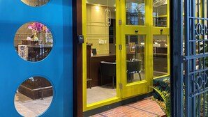 A brightly colored entrance with a yellow door, a blue wall with circular windows, and a welcome mat. - Chomm House (Bangkok)