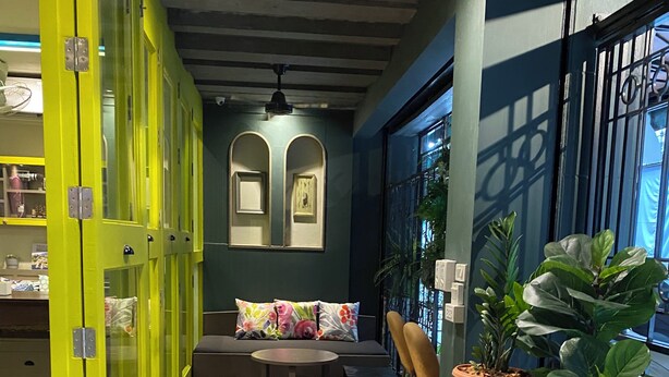 A cozy indoor seating area with a tiled floor, a sofa with floral cushions, and potted plants. - Chomm House (Bangkok)