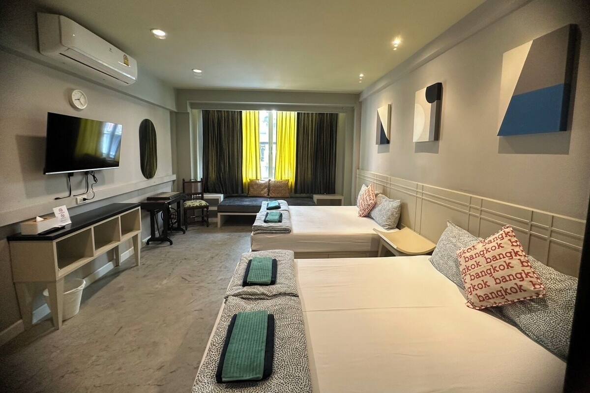 A hotel room with two beds, a TV, a desk, and a window with curtains.