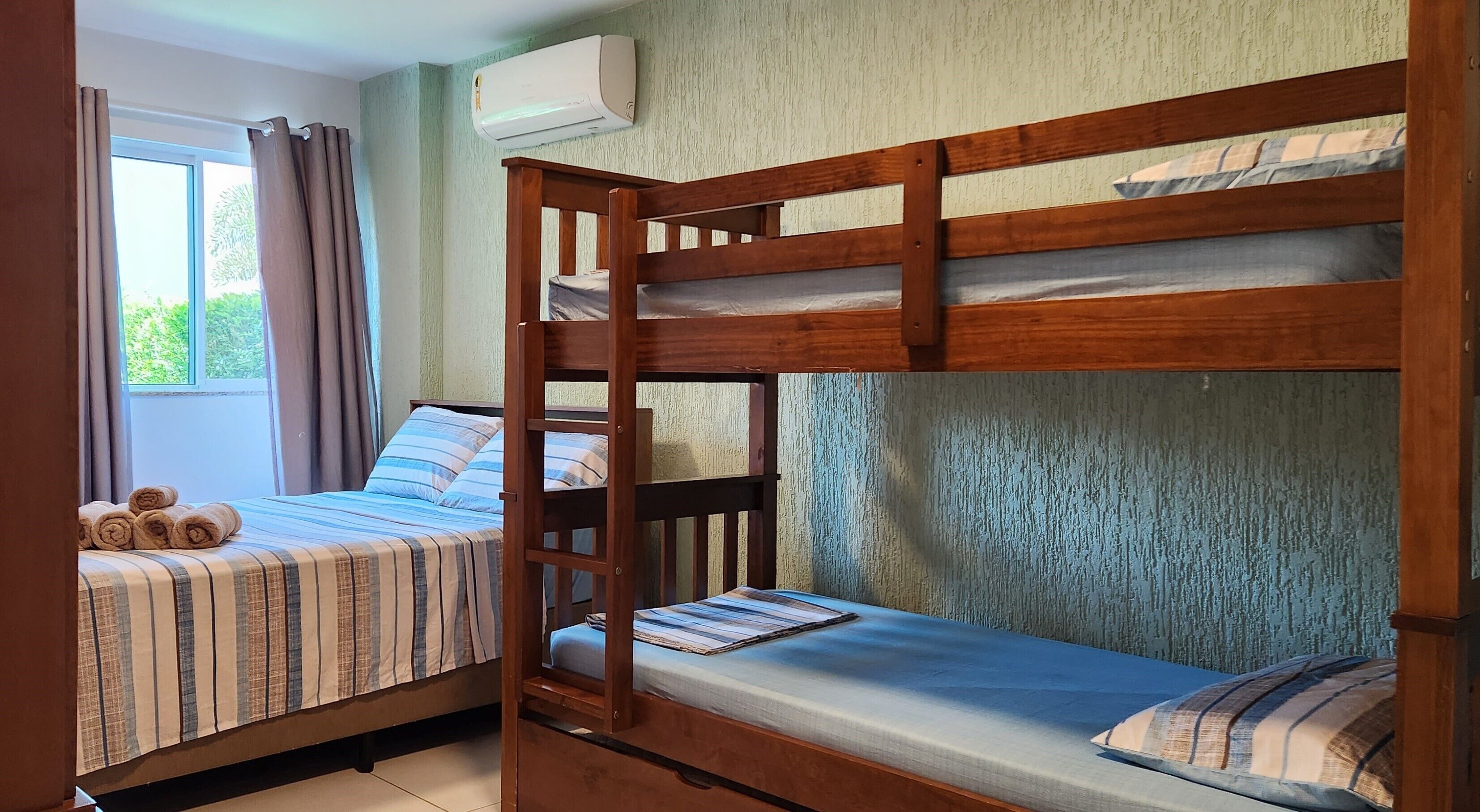 Quarto com duas beliches, uma janela com cortinas e um aparelho de ar condicionado.