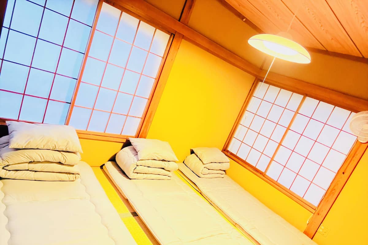 A room with two beds, a wooden ceiling, and a window with a grid pattern.