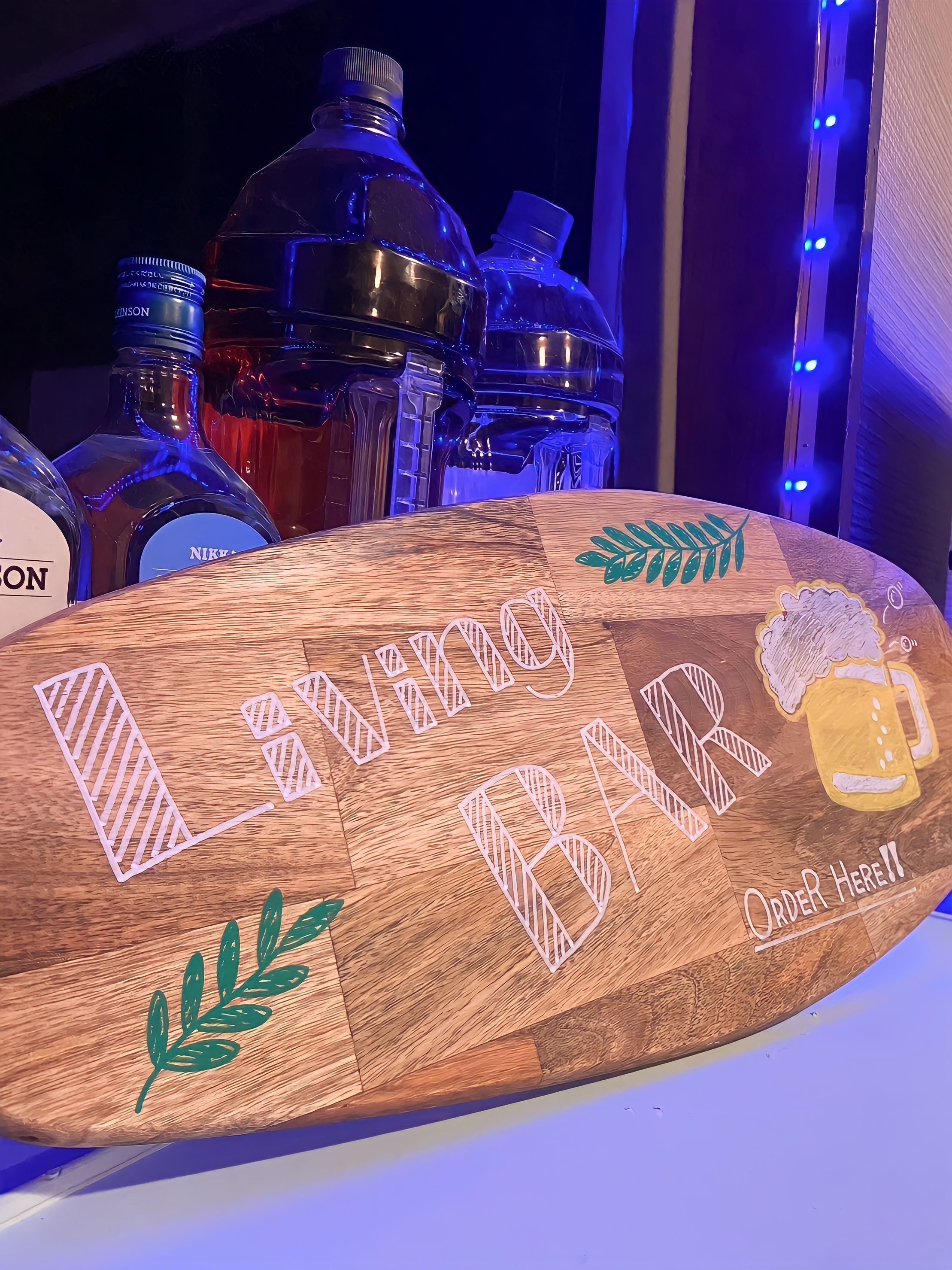 A wooden sign with cut-out letters spelling "BAR" and "Order Here!!" with decorative elements like leaves and a beer mug.