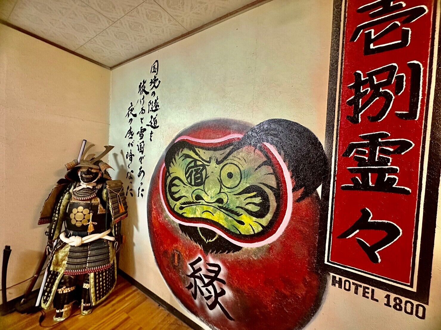 A wall with a large red and black painting of a face, a samurai figure, and Japanese text.