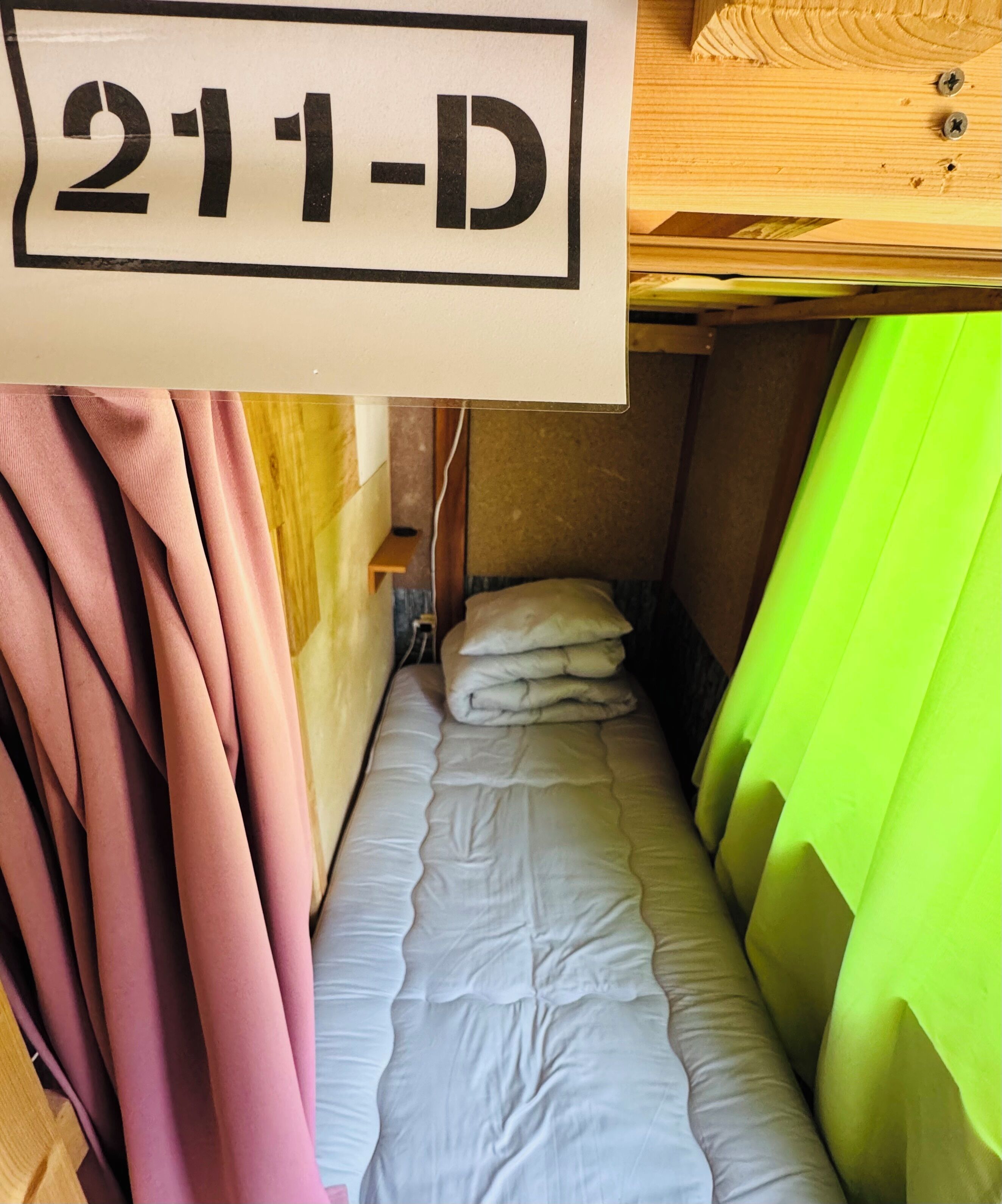 A small, narrow room with a bunk bed and a sign above indicating room number 211-D.