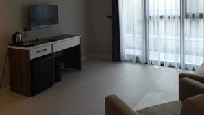 Una sala de estar moderna con televisor de pantalla plana, un escritorio y un ventanal con cortinas translúcidas.