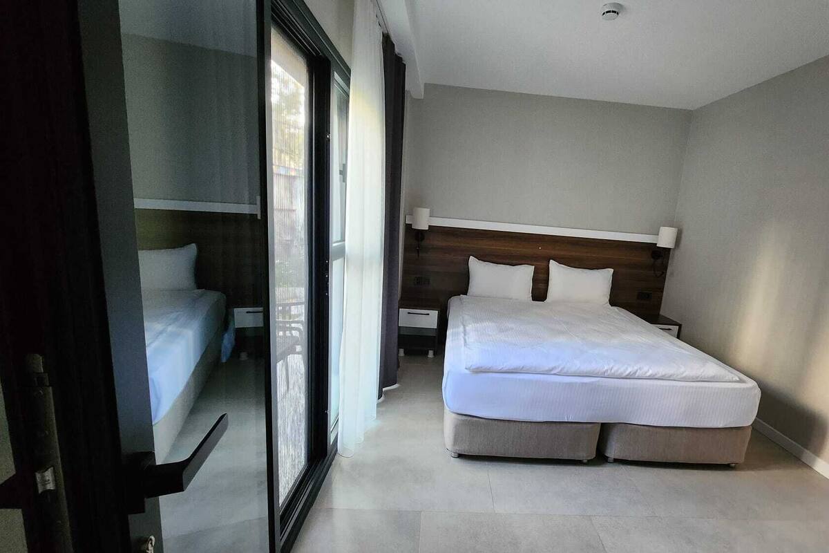 A modern bedroom with a large bed, a nightstand, a wooden headboard, and a sliding glass door leading to another room.