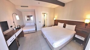 Habitación de hotel con una cama grande, un escritorio con silla, televisión y mesita de noche con lámpara.