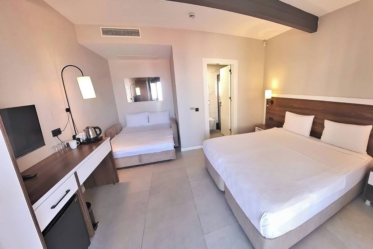 A hotel room with a large bed, a desk with a chair, a TV, and a bedside table with a lamp.