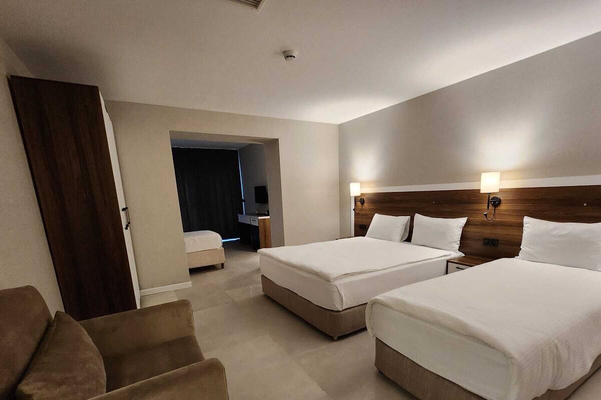 A hotel room with two beds, a sofa, a desk, and a TV.