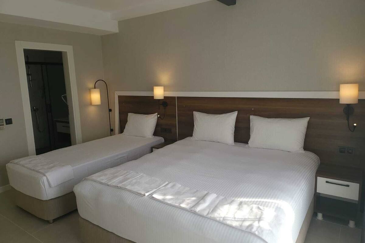 A hotel room with two single beds, a wooden headboard, bedside lamps, and a nightstand with a drawer.
