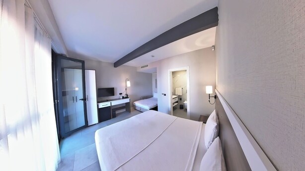 Habitación de hotel con una cama grande, un escritorio, un televisor y un baño visible a través de una puerta abierta.