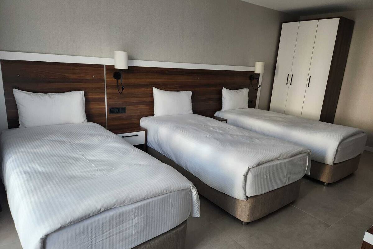 A hotel room with three single beds, a wooden headboard, a wardrobe, and a bedside table with a lamp.
