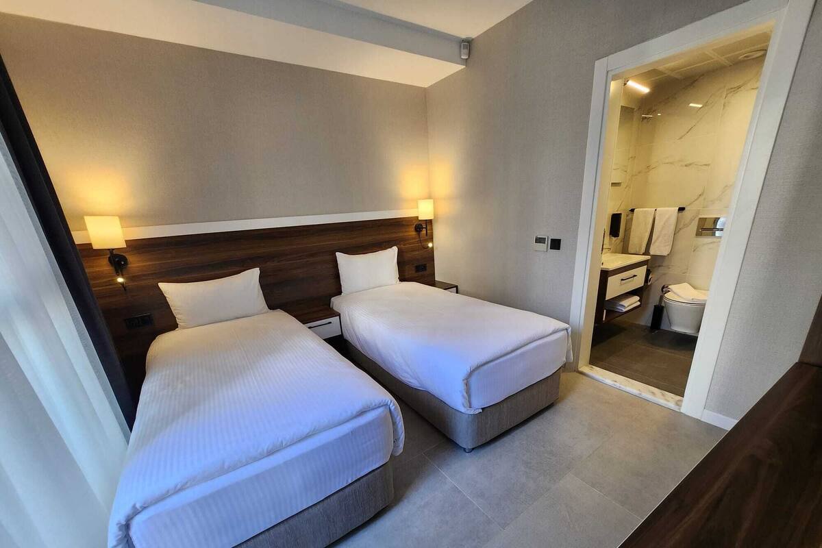 A hotel room with two beds, a wooden headboard, a bathroom with a marble wall, and a small desk.