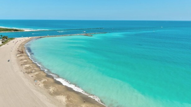 An aerial view of a beach with clear turquoise waters, a sandy shore, and a breakwater structure. - 404 Ocean View Condo (Avalon Beach Club Assn) (Fort Pierce)