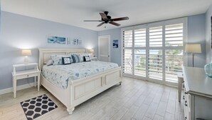 A bedroom with a bed, a ceiling fan, a window with blinds, and a nightstand with a lamp. - 404 Ocean View Condo (Avalon Beach Club Assn) (Fort Pierce)