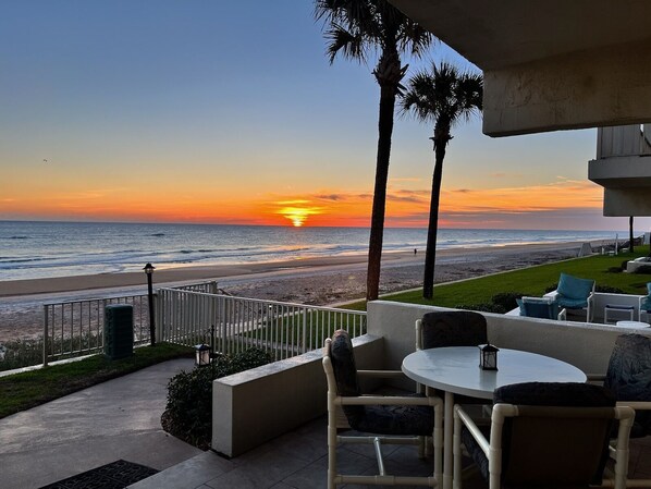 Un patio frente a la playa con mobiliario exterior, vista al océano y palmeras.