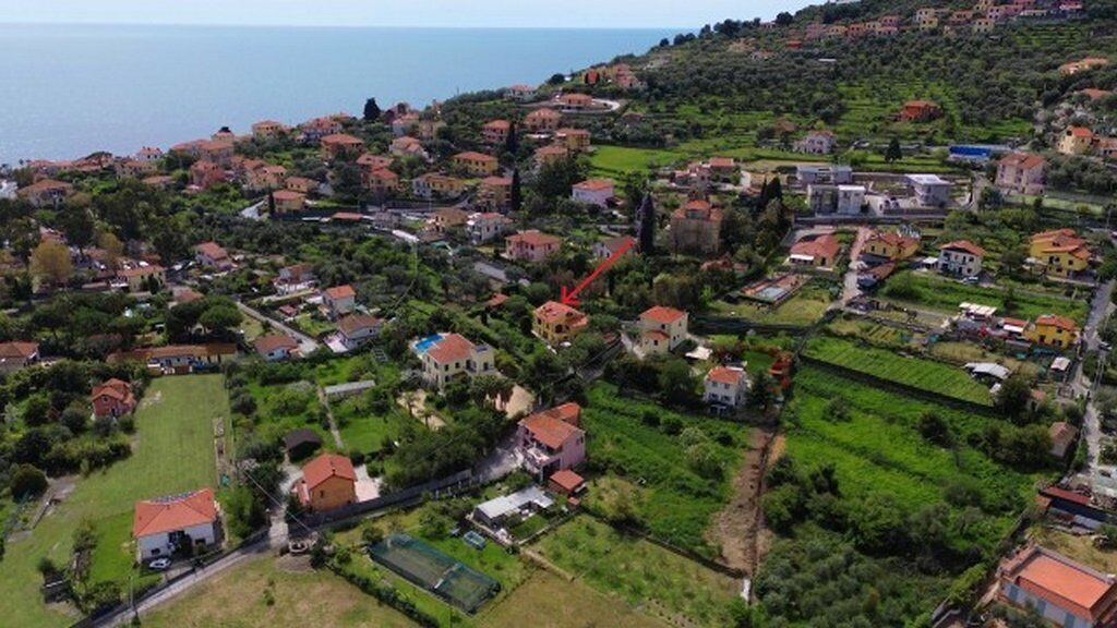 Vista aérea de un pueblo costero con casas, campos verdes y una carretera que lleva al mar.