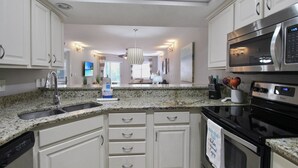 Cozinha moderna com bancadas de granito, eletrodomésticos de aço inoxidável e armários brancos.