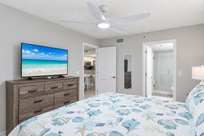 A bedroom with a bed, a TV on a dresser, a ceiling fan, and a bathroom with a shower.