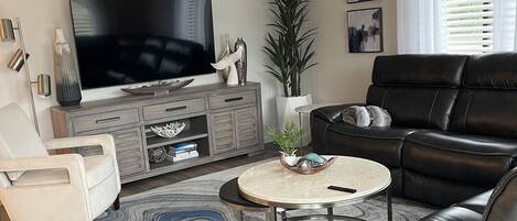 A modern living room with a flat-screen TV, leather sofa, and a ceiling fan.