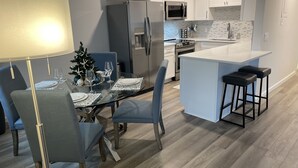 A modern kitchen with white cabinets, a stainless steel refrigerator, a microwave, and a sink. There is a dining table with chairs and a small Christmas tree. - Newly renovated Lantana FL condo, All new luxury furnishings, 2 miles from Ocean (Lantana)