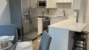 A modern kitchen with white cabinets, stainless steel appliances, and a central island with bar stools. - Newly renovated Lantana FL condo, All new luxury furnishings, 2 miles from Ocean (Lantana)