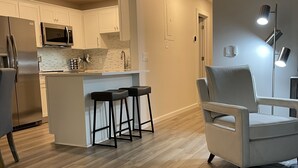 A modern kitchen with white cabinets, a stainless steel refrigerator, a microwave, and a bar area with stools. - Newly renovated Lantana FL condo, All new luxury furnishings, 2 miles from Ocean (Lantana)