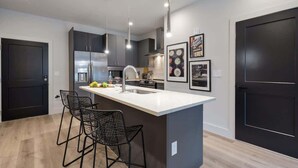 Una cocina moderna con una isla central, taburetes de bar, iluminación colgante y cuadros en la pared.