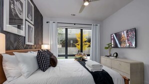 Una habitación de hotel moderna con cama, televisor, mesita de noche, cómoda y ventana con cortinas.